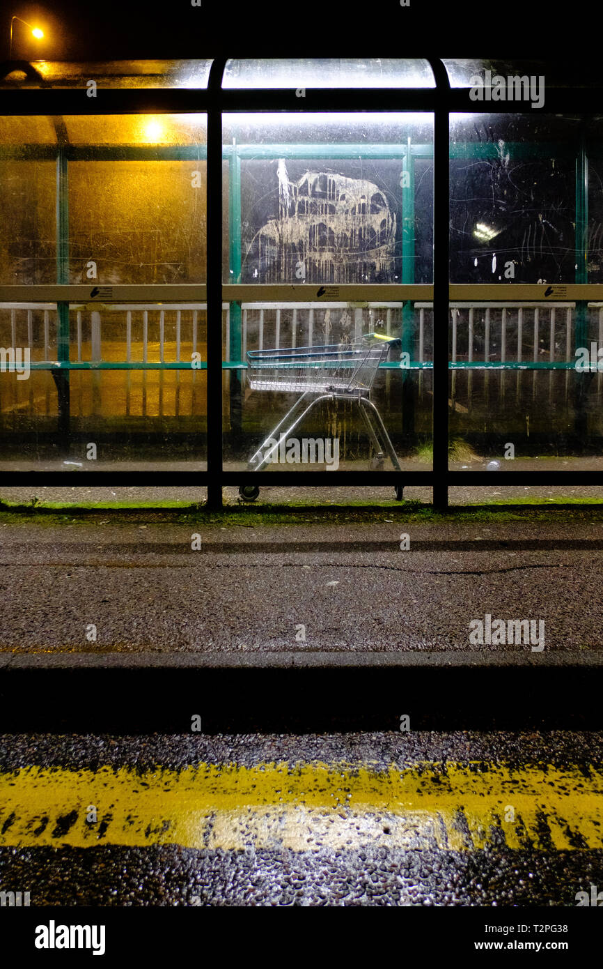 Un carrello trolley giace abbandonata all'interno di un bus un riparo in una umida notte scozzese Foto Stock