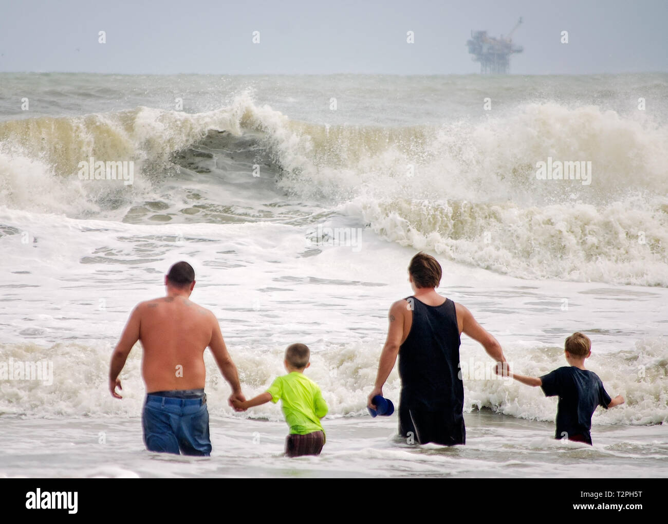 Padri tenere le mani con i loro figli come essi svolgono in onde calci fino dalla tempesta tropicale Gordon in Dauphin Island, Alabama. Foto Stock