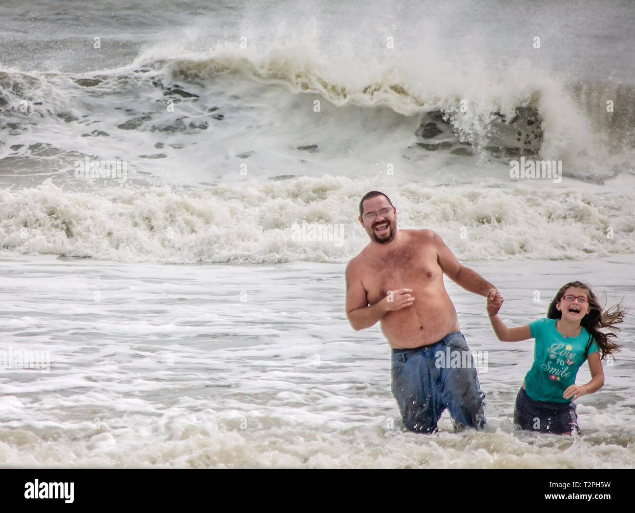 Un padre e figlia ridere come essi svolgono le onde calci fino dall'approccio della tempesta tropicale Gordon Foto Stock