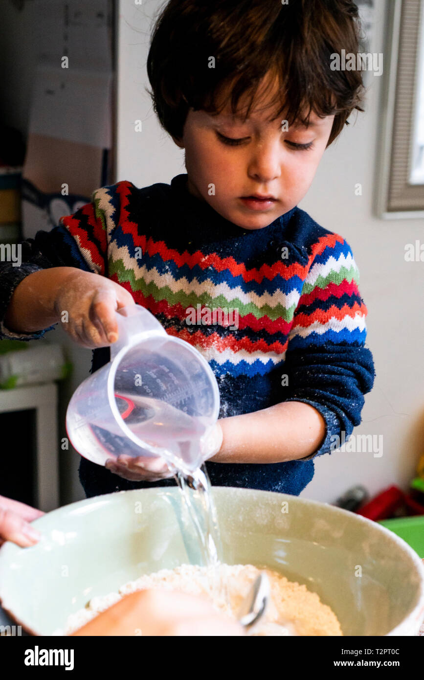 Il Toddler versare acqua in farina nel recipiente di miscelazione Foto Stock