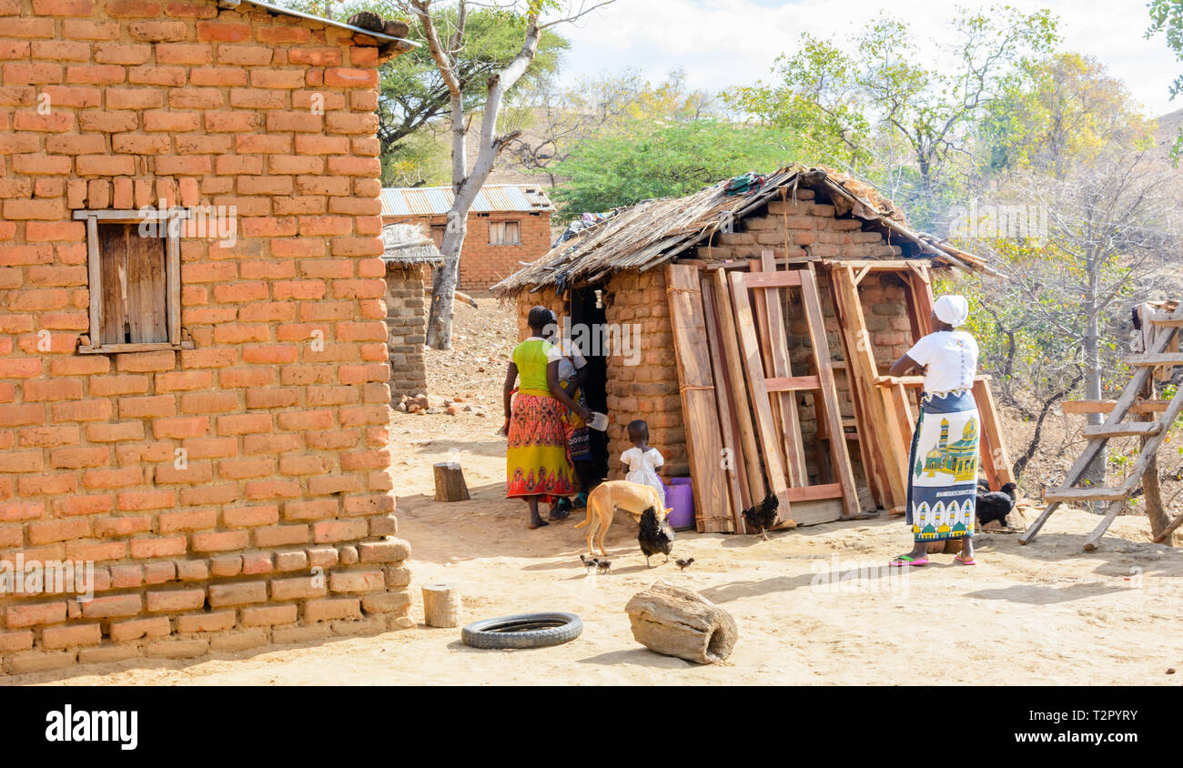 Villaggio del Malawi carpenter impilati i suoi telai di porte e finestre contro la parete di erba con tetti cucina Foto Stock