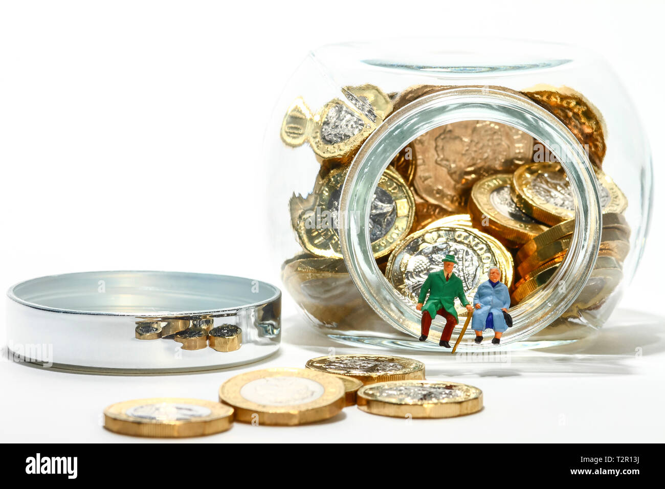 Diorama concettuale immagine di anziani figure in miniatura seduto sul bordo di un vasetto di vetro pieno di libbra di monete Foto Stock
