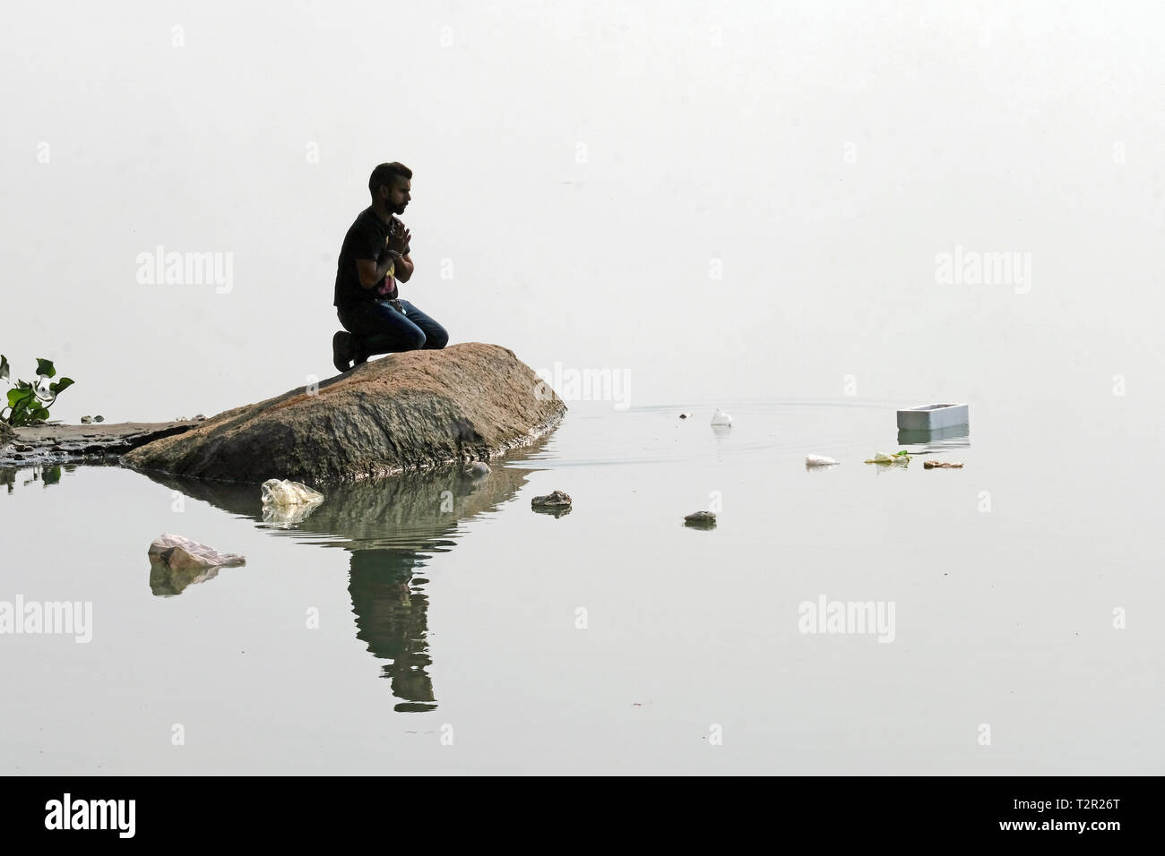 Un uomo è in preghiera su una roccia nel fiume inquinato Brahmaputra in Tezpur, stato di Assam, in India Foto Stock