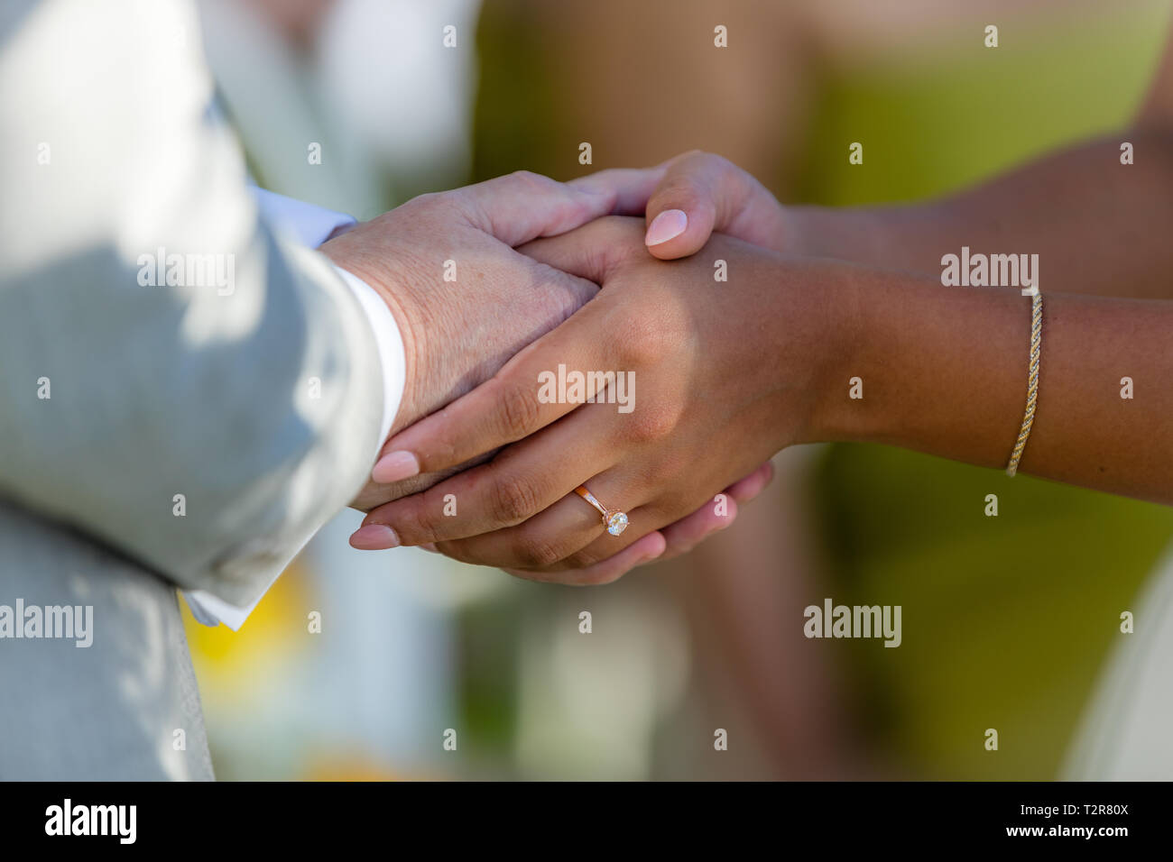 Sposa e lo sposo tenendo le mani dopo una cerimonia di matrimonio. Il meticciato - uomo caucasico e donna asiatica. Foto Stock