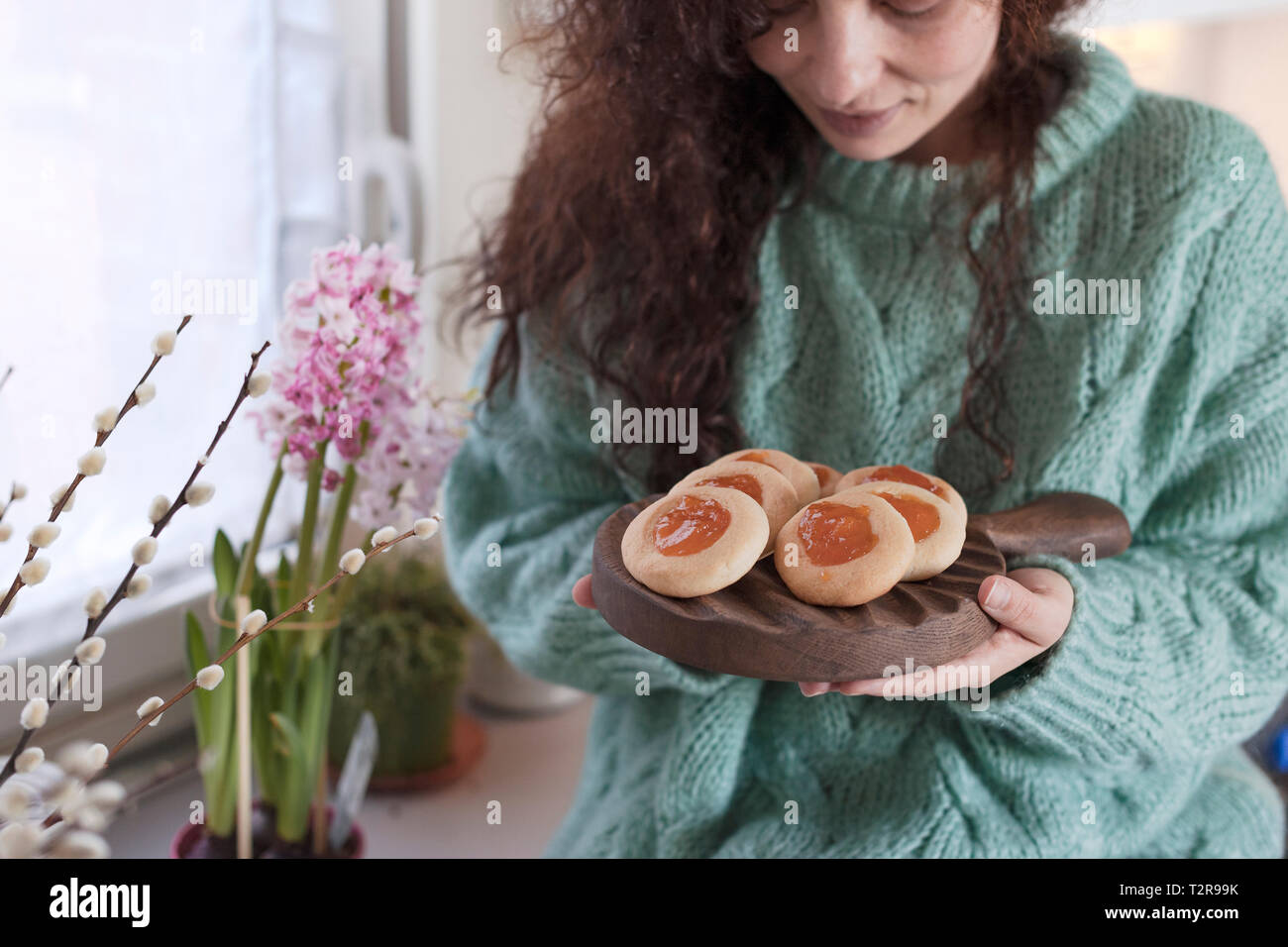 Donna con biscotti e caffè nella cucina. La prima colazione e i fiori sul tavolo da finestra con la ragazza. Concetto di comfort e hipster, Foto Stock