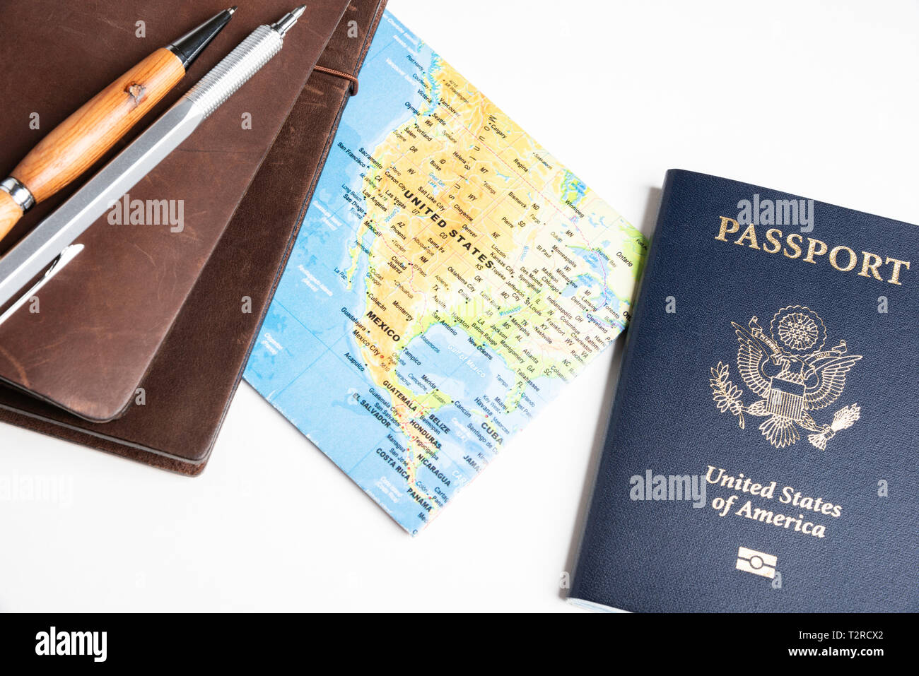 Un college americano di copertura blu passaporto con un mondo ripiegato mappa, riviste in pelle e set di penne su una pianura solido sfondo bianco. Foto Stock