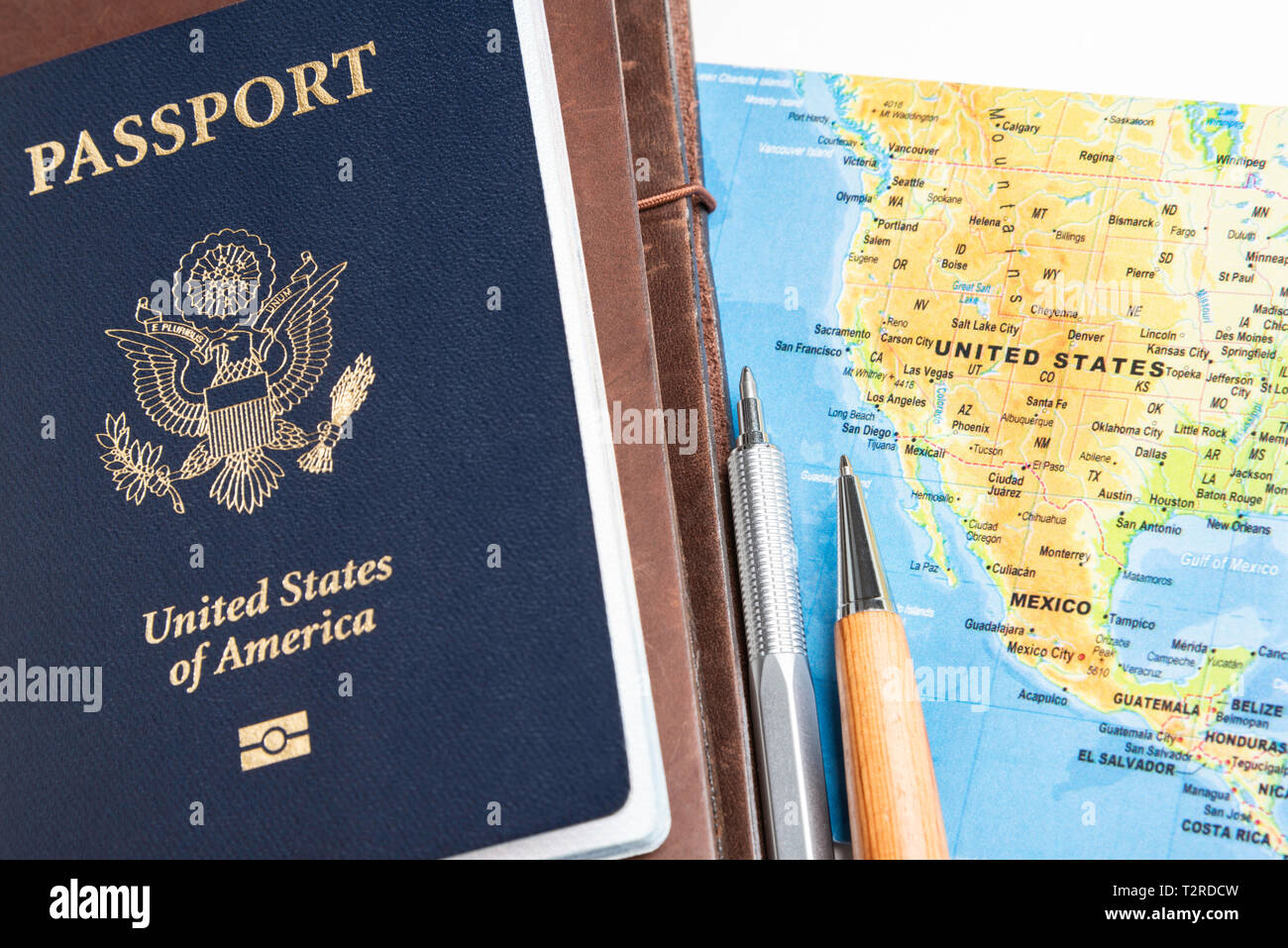 Un college americano di copertura blu passaporto con un mondo ripiegato mappa, riviste in pelle e set di penne su una pianura solido sfondo bianco. Foto Stock