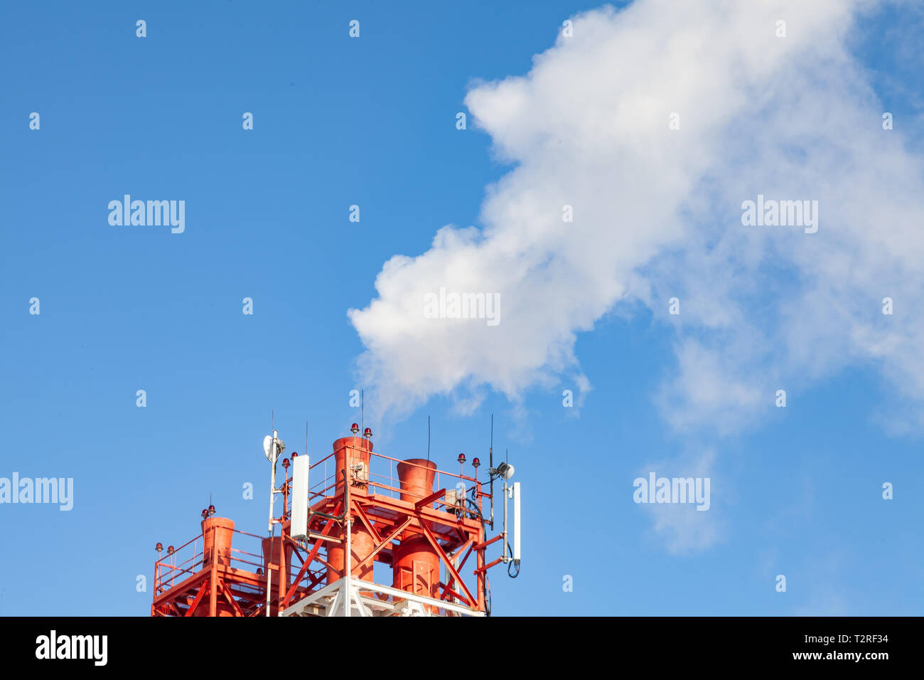 White nocivi del fumo proveniente al di fuori del rosso-e-bianco con tubi di comunicazione mobile antenne in una fabbrica nel centro della città contro lo sfondo di Foto Stock