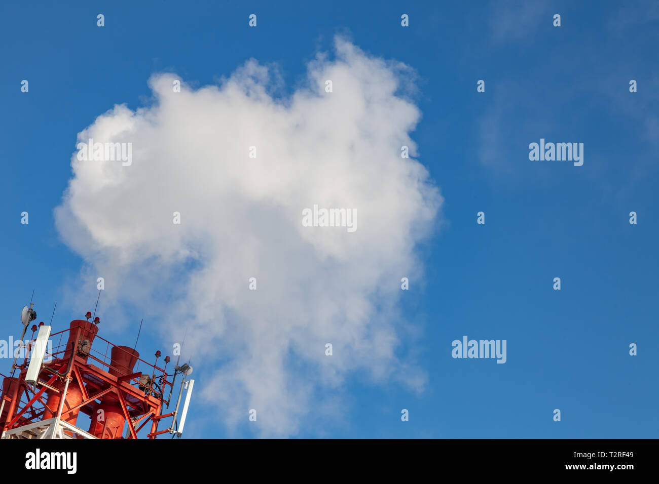 White nocivi del fumo proveniente al di fuori del rosso-e-bianco con tubi di comunicazione mobile antenne in una fabbrica nel centro della città contro lo sfondo di Foto Stock