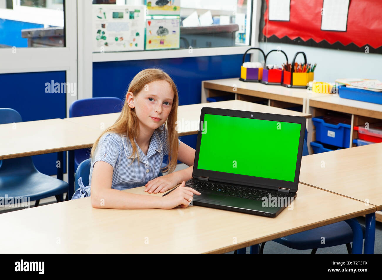 La scuola primaria caucasian ragazza con il suo computer portatile con uno schermo verde Foto Stock