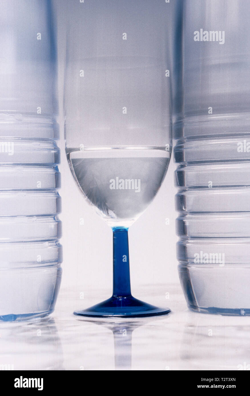 Bicchiere di acqua tra due bottiglie di plastica Foto Stock
