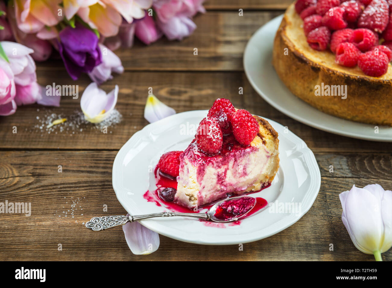 Fetta di casalinghe Cheesecake alla vaniglia con lamponi e salsa di frutti di bosco scuri su sfondo rustico Foto Stock
