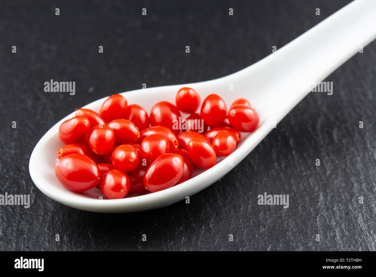 Fresche bacche di goji in una piccola porcellana bianca cucchiaio isolato sul buio spazio copia closeup Foto Stock