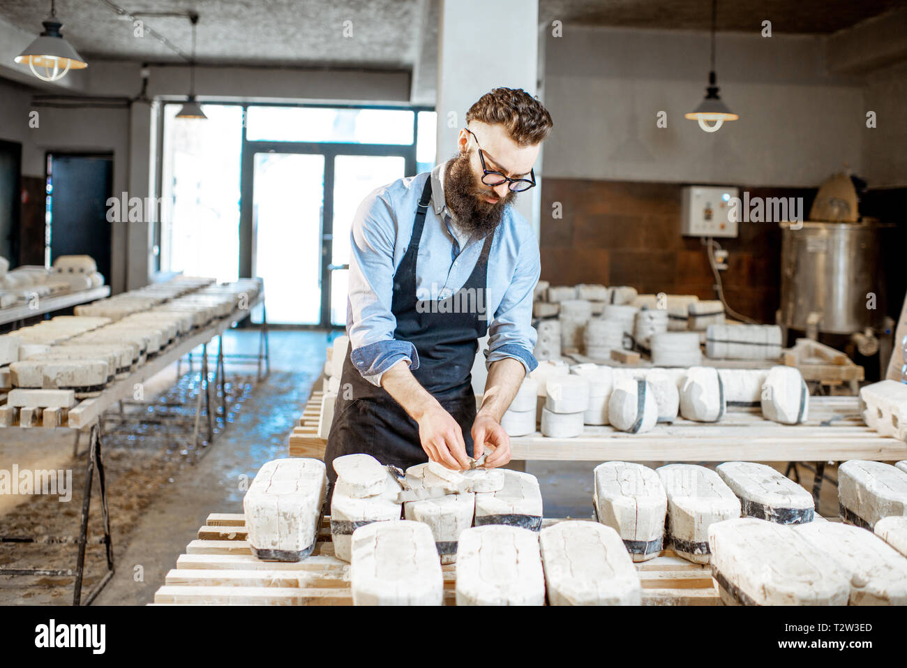 Bello il lavoratore nel grembiule ottenendo prodotti di argilla dalle forme di gesso alla Fabbricazione ceramica Foto Stock