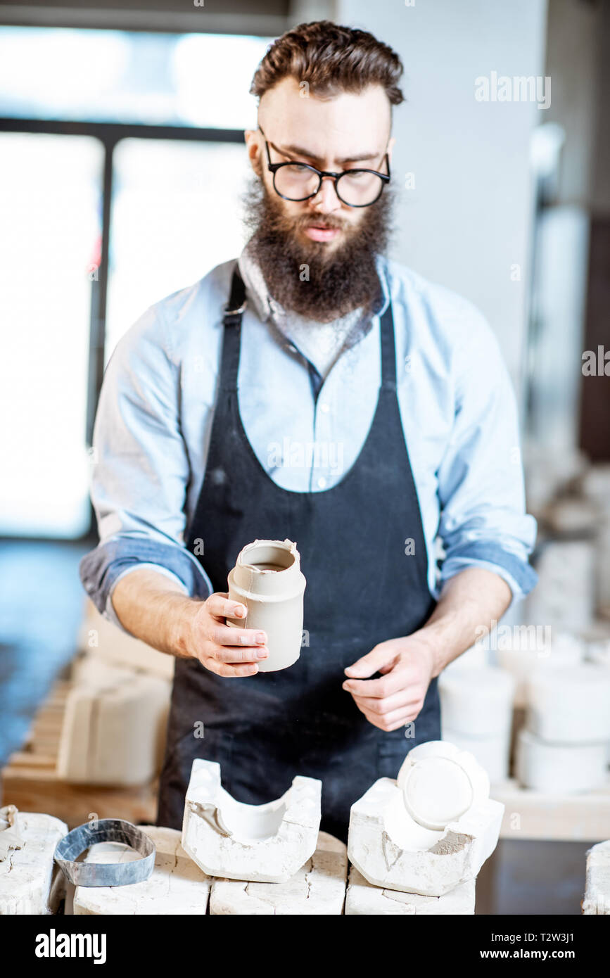 Bello il lavoratore nel grembiule ottenendo prodotti di argilla dalle forme di gesso alla Fabbricazione ceramica Foto Stock