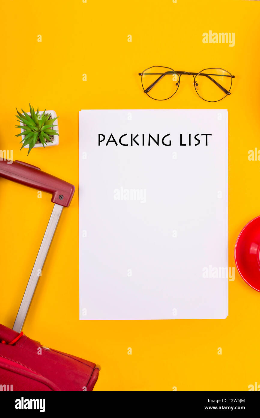 La lista di imballaggio per il viaggio è prossima ad una valigia, una tazza di caffè e una cannuccia estate borsa su uno sfondo giallo. Tenetevi pronti per un concetto di viaggio Foto Stock