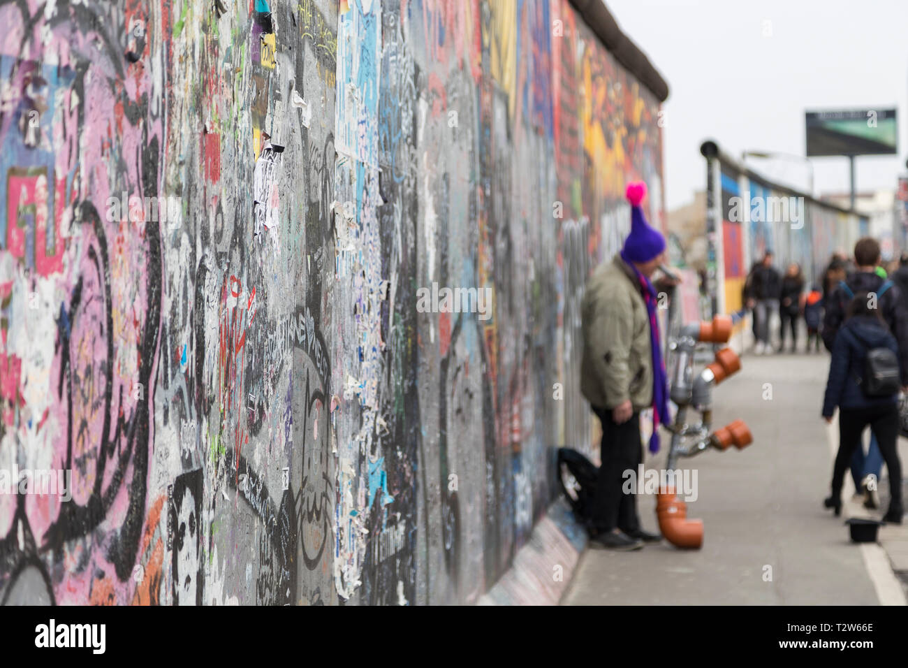 Close-up di graffiti presso la East Side Gallery, la sezione del muro di Berlino in Berlino, Germania. Musicista di strada e turisti in background. Foto Stock