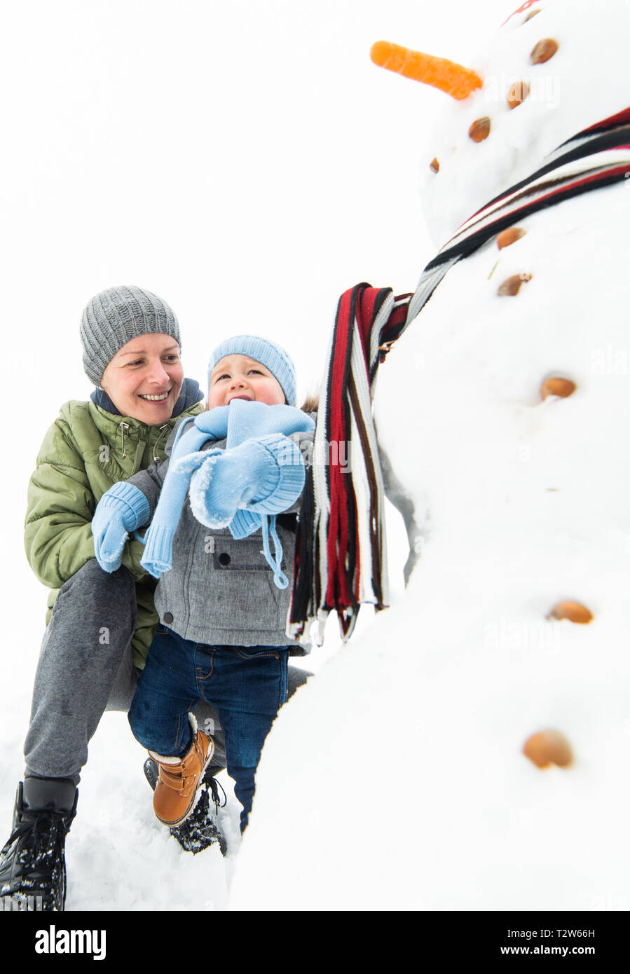 Sorridente baby boy e di sua madre la costruzione di pupazzo di neve nel Parco Foto Stock