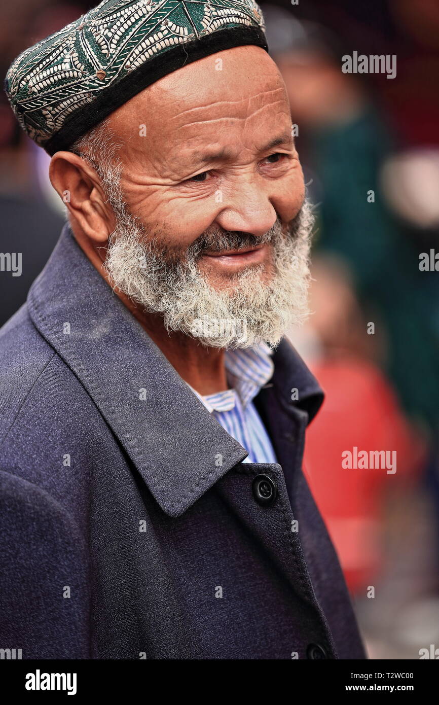 Uomo bearded Uyghur che indossa doppa-skullcap al bazar della città. Hotan-Xinjiang-Cina-0076 Foto Stock