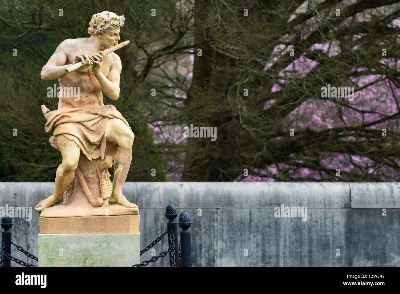 La terracotta statua chiamata Fauno svolge un tubo contro uno sfondo di alberi e cespugli fioriti, al Biltmore House di Asheville, NC, Stati Uniti d'America Foto Stock