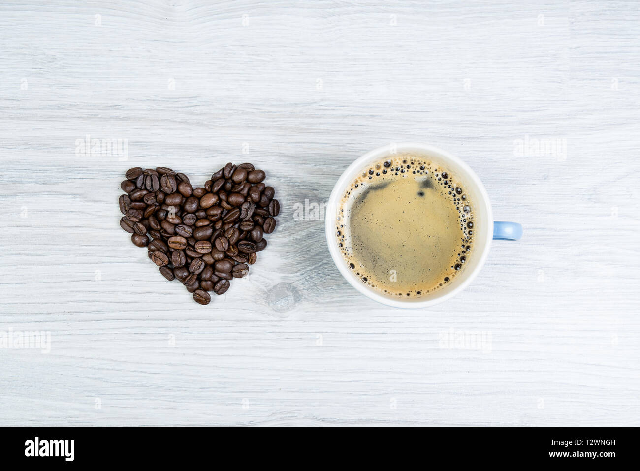 Amore caffè, a forma di cuore fatto di chicchi di caffè accanto a una tazza di caffè su di un tavolo di legno. può essere usata come sfondo Foto Stock
