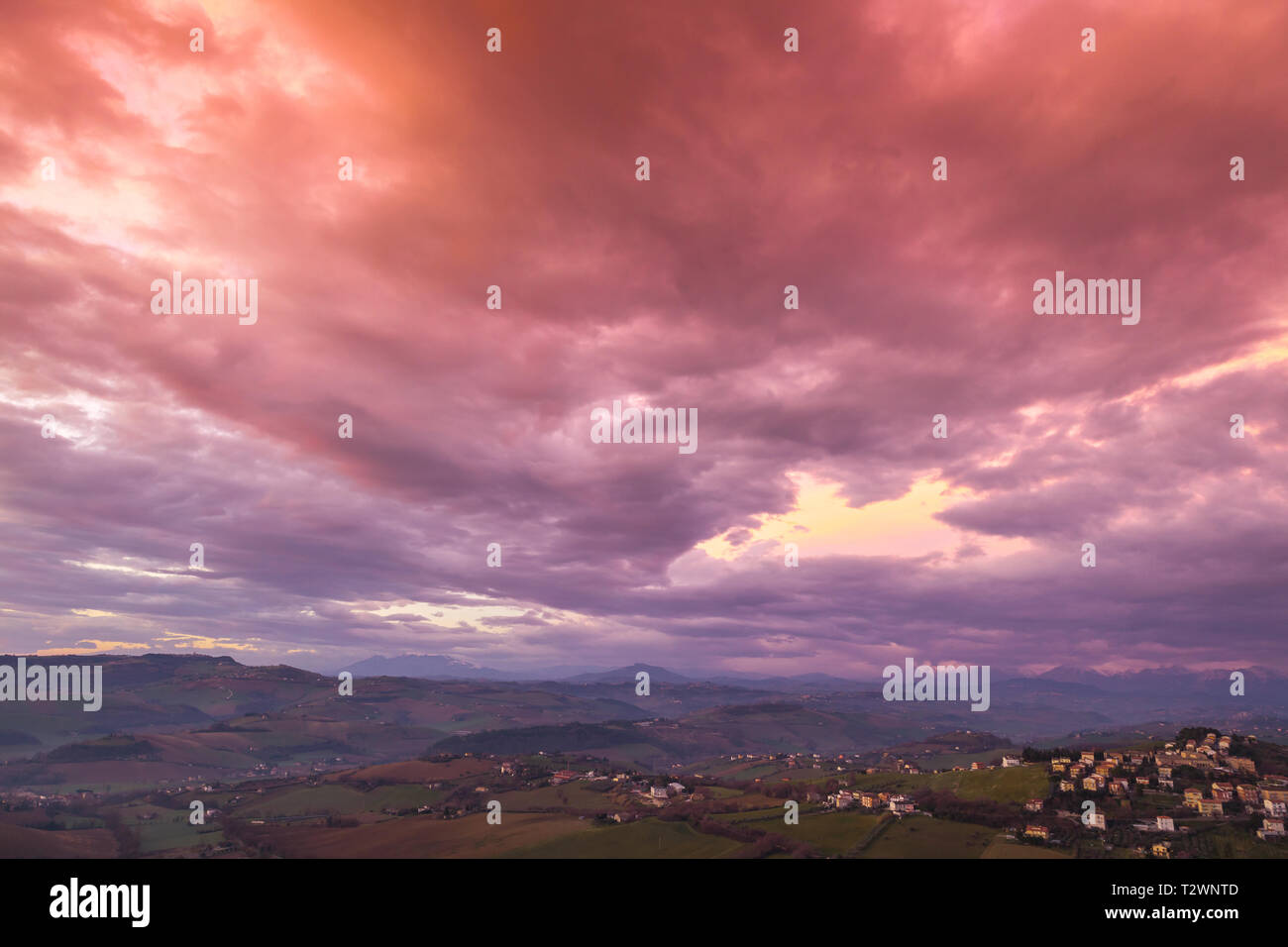 Campagna Italiana, paesaggio rurale. Provincia di Fermo, Italia. Villaggio sulla collina sotto red cielo molto nuvoloso Foto Stock