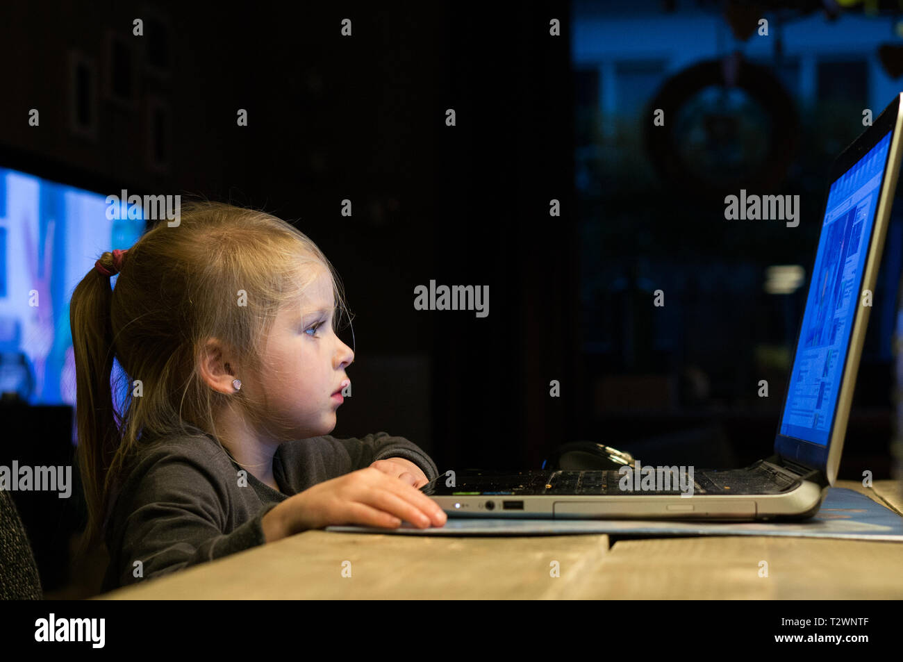 Carino giovane ragazza sta usando un computer portatile a casa. Un giovane bambino con la tecnologia Foto Stock