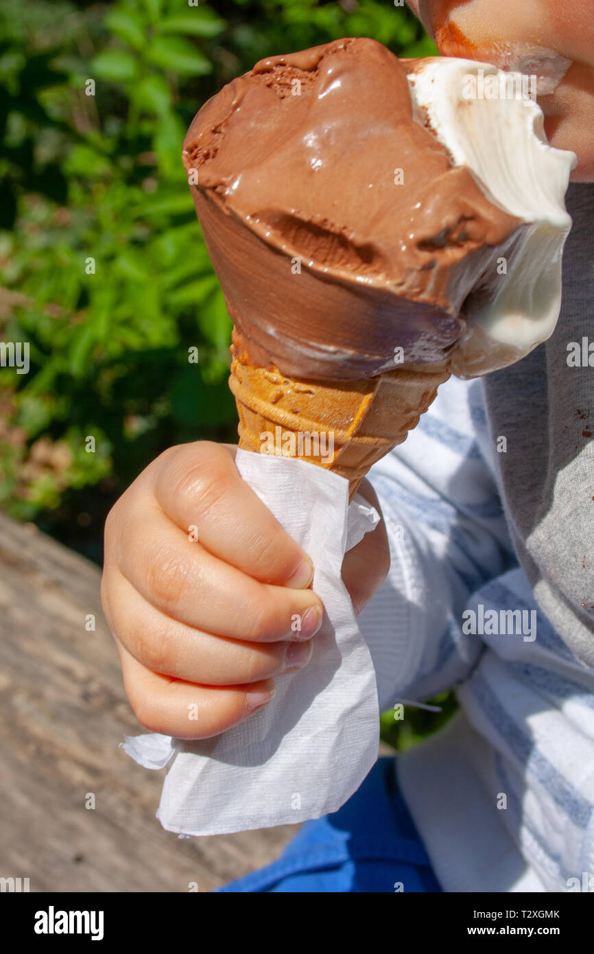 Carino bambino mangiare cioccolato cono gelato in estate in un parco. Ragazzino, piccola mano, senza volto, close up Foto Stock