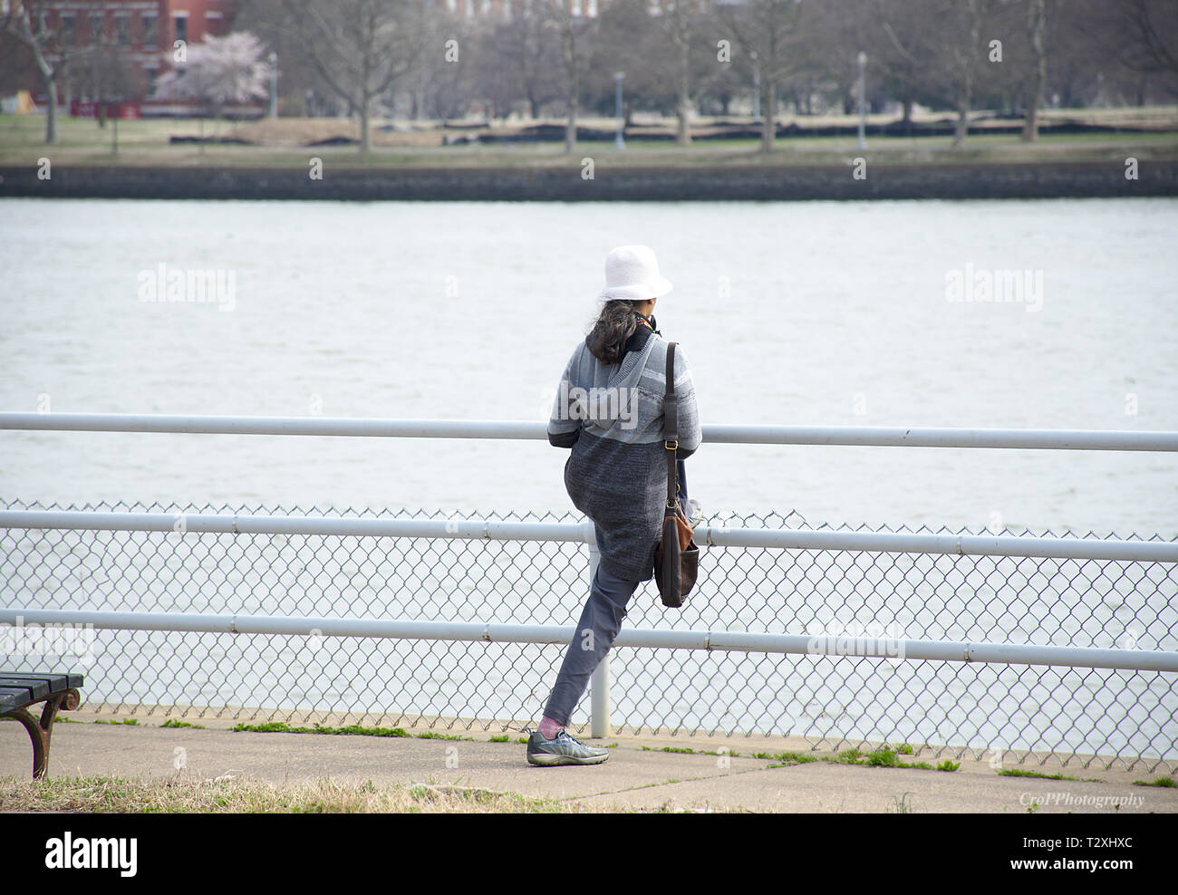 Vista posteriore della femmina con un cappello bianco trasporto borsa a mano il suo allungamento della gamba sul parapetto Foto Stock