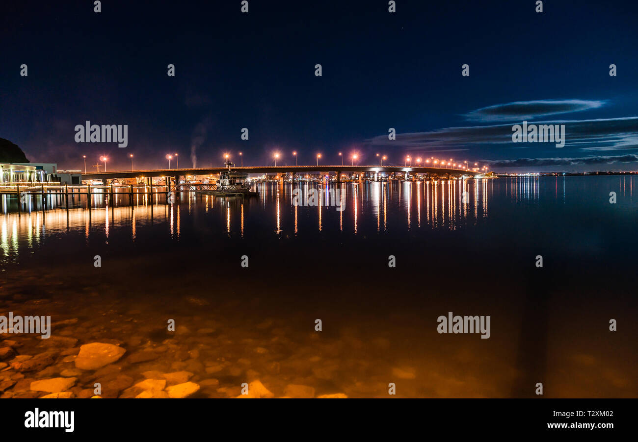 Tauranga Harbour Bridge accese le luci di strada sopra e luci della città al di sotto di notte Foto Stock