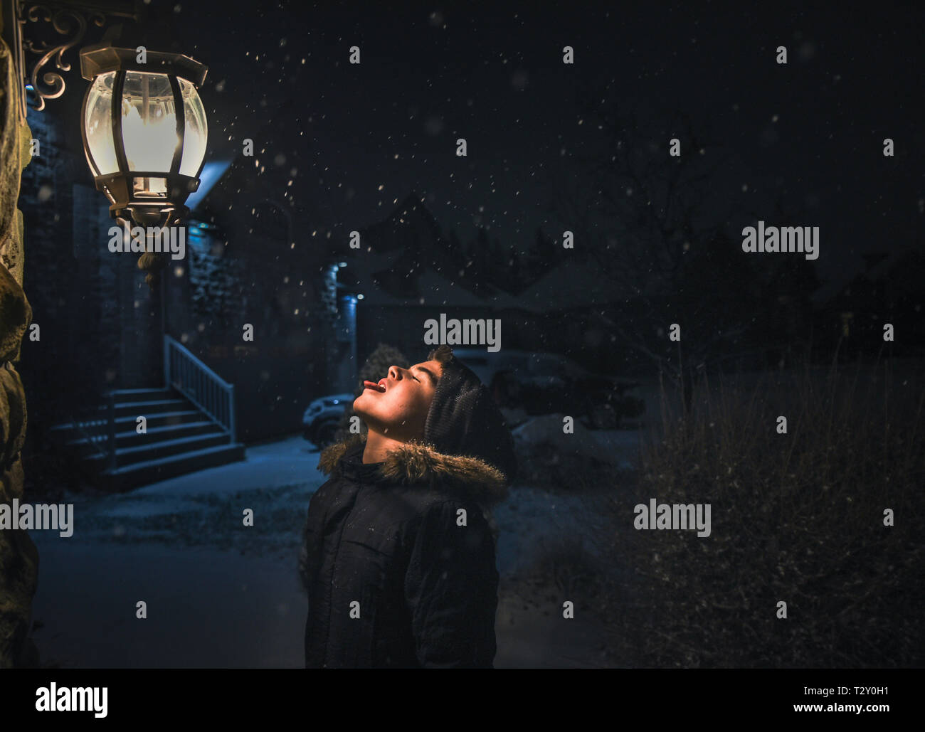Ragazzo cattura i fiocchi di neve sulla sua linguetta accanto a una luce su una notte nevosa Foto Stock