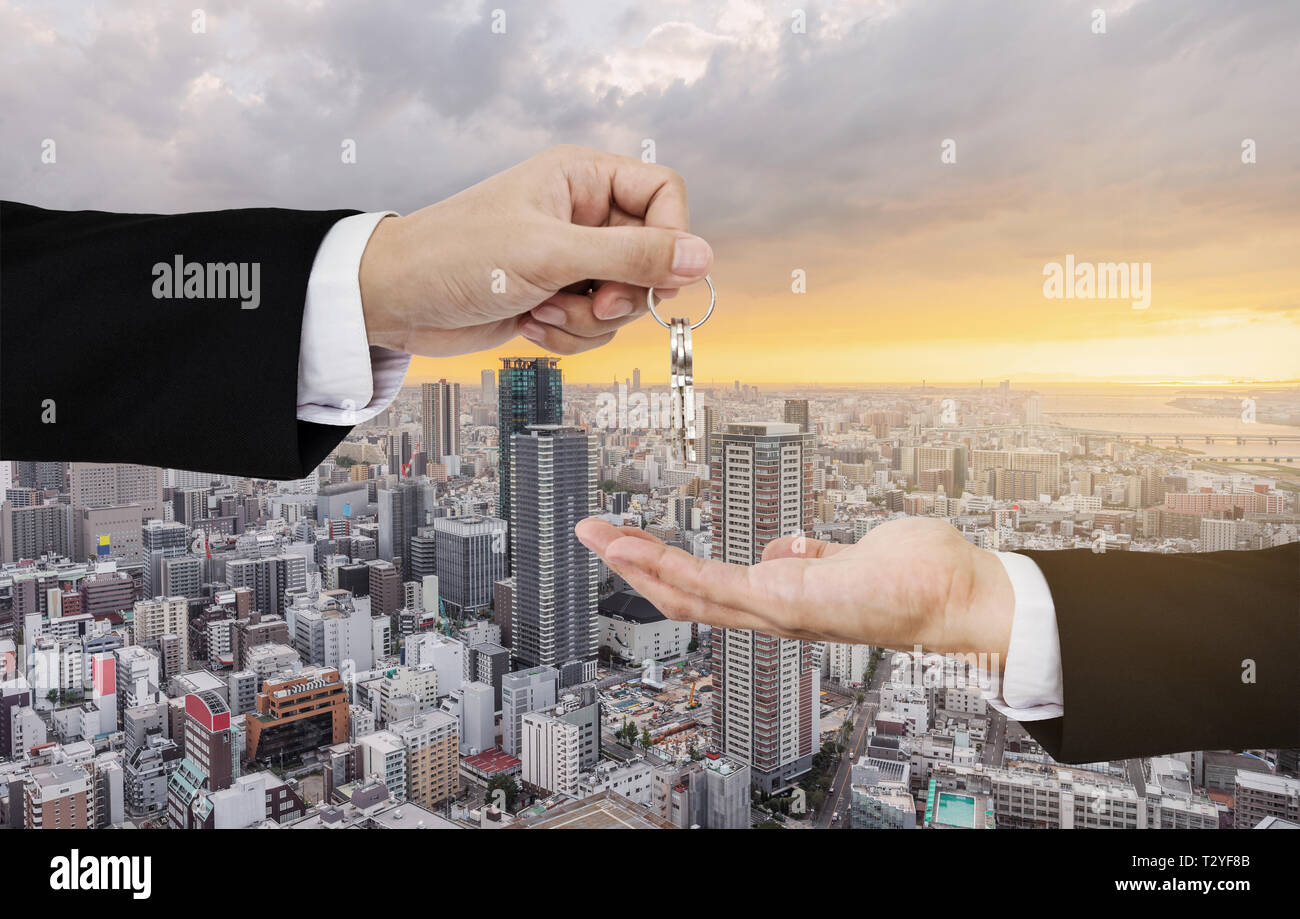 Attività immobiliari, noleggio residenziale e degli investimenti. Imprenditore tasti di handover, con la città sullo sfondo di sunrise Foto Stock