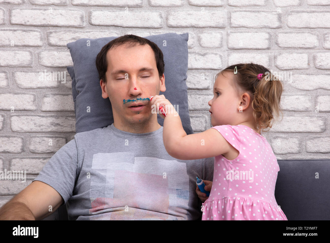 Bambina pittura volto del Padre mentre egli dorme sul divano di casa Foto Stock