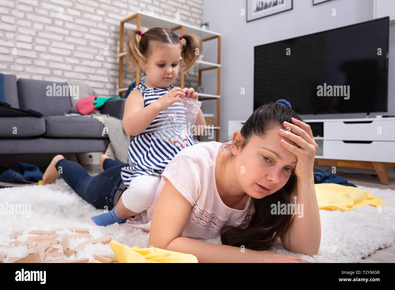 Felice maliziosa ragazza che gioca con il suo stanco madre giacente su un tappeto Foto Stock