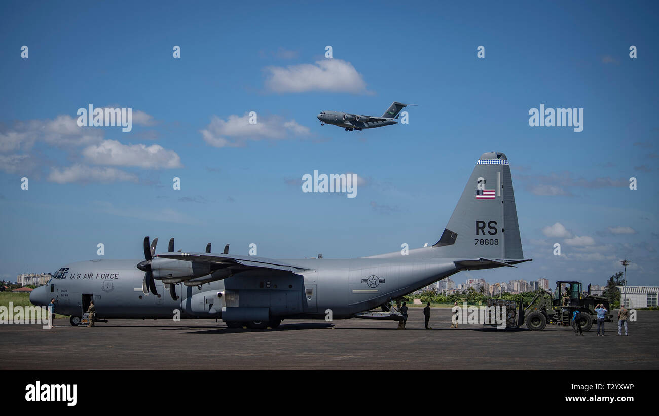 Un U.S. Air Force C-17 assegnato al XVI Airlift Wing, Base comune Charleston, Charleston, Carolina del Sud è in avvicinamento finale come un U.S. Air Force C-130J Hercules assegnato al settantacinquesimo Expeditionary Airlift Squadron, Combined Joint Task Force-Horn dell Africa (CJTF-HOA) è caricato con aiuti internazionali delle Nazioni Unite per i bambini del fondo di emergenza (UNICEF), all'aeroporto di Maputo, Mozambico, 4 aprile 2019. La task force è soddisfare le esigenze identificate da USAID squadre di valutazione e le organizzazioni umanitarie che operano nella regione fornendo supporto logistico e di manodopera per gli Stati Uniti Foto Stock