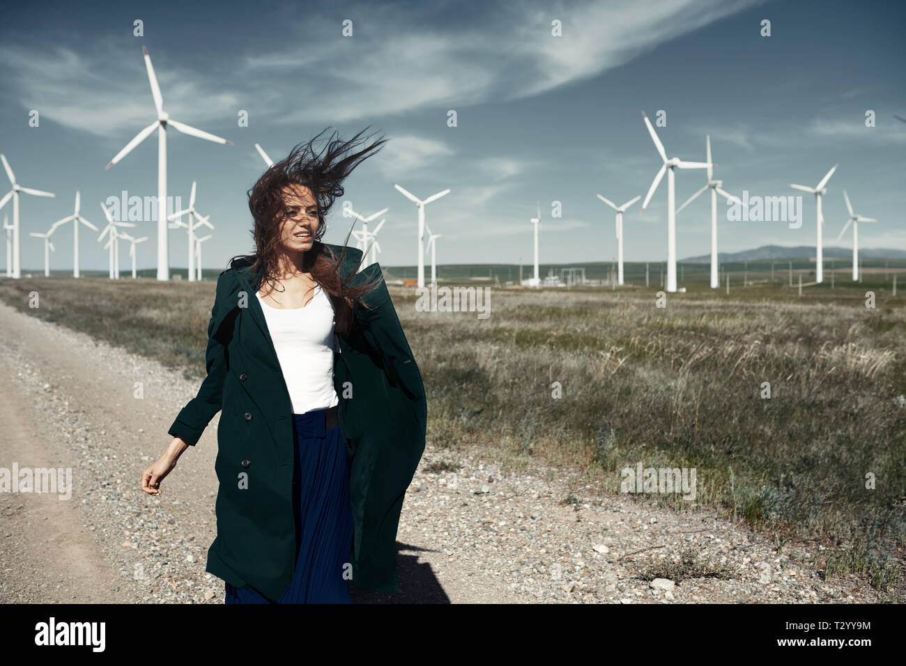 Donna con lunghi capelli tousled accanto alla turbina eolica con il vento che soffia Foto Stock