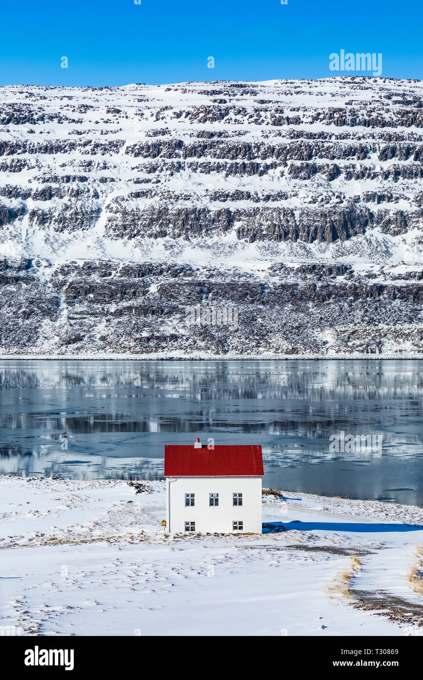 Casa con il tetto rosso nel drammatico paesaggio invernale lungo il fiordo Ísafjarðardjúp nei pressi di Ísafjörður nella regione Westfjords, Islanda [alcuna proprietà di rilascio; av Foto Stock