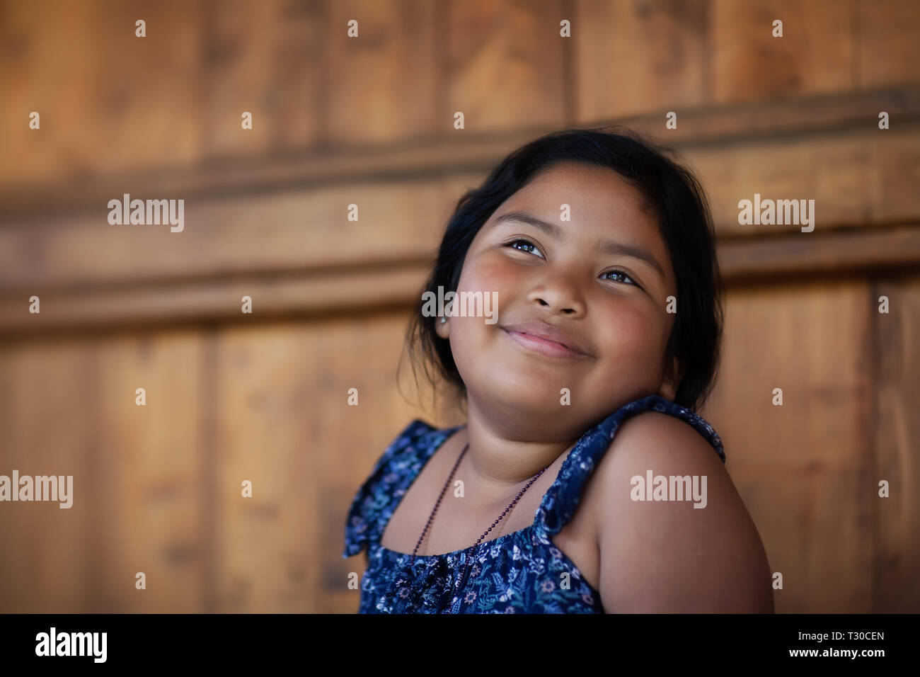 Giovane ragazza etnica di ricordare un momento felice nella sua mente e di esprimere la gioia attraverso un sorriso e gli occhi luminosi. Foto Stock