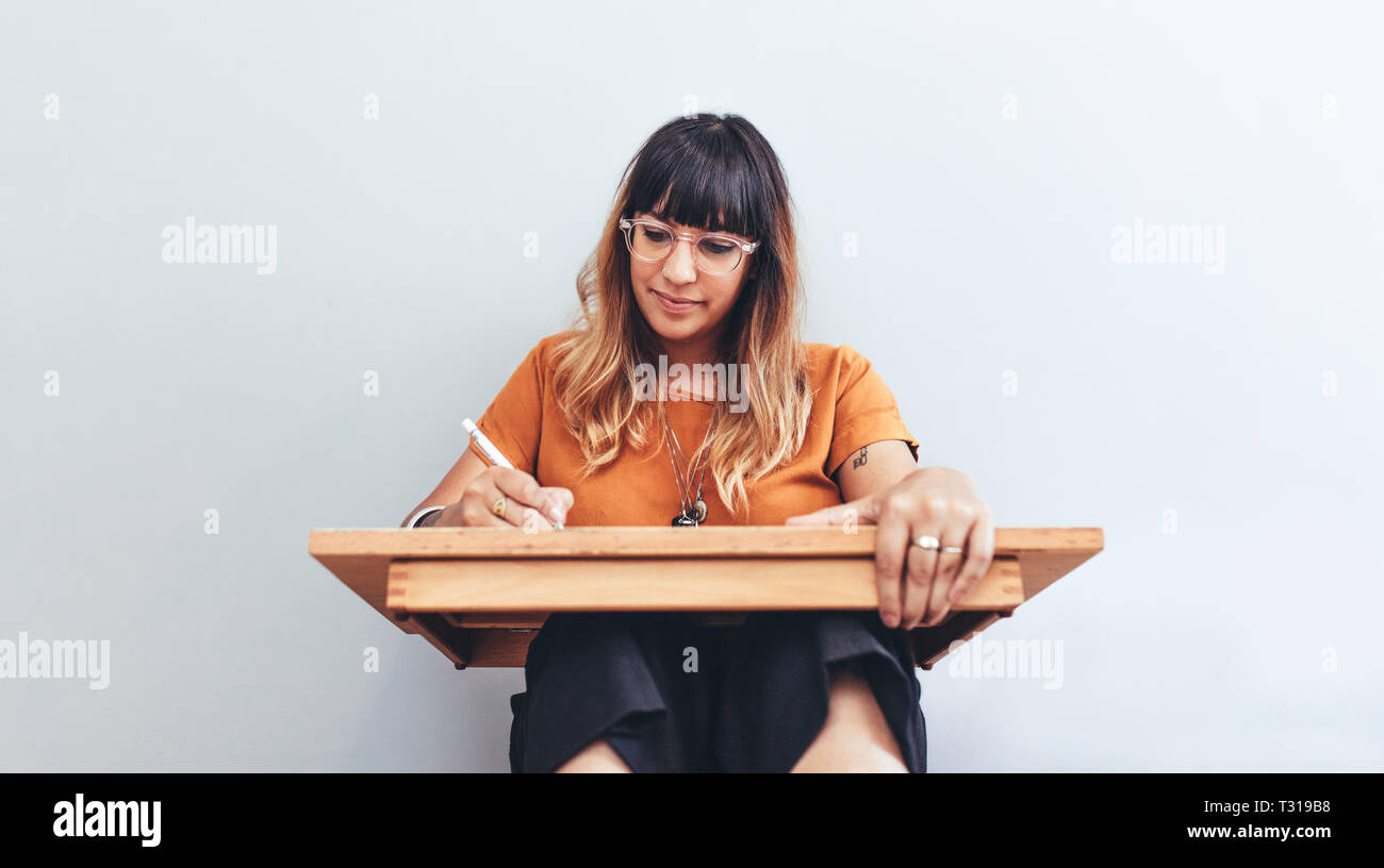 Ritratto di una donna seduta sul pavimento con un tampone di disegno facendo uno schizzo. Close up di un artista creativa al lavoro di disegno di un disegno. Foto Stock
