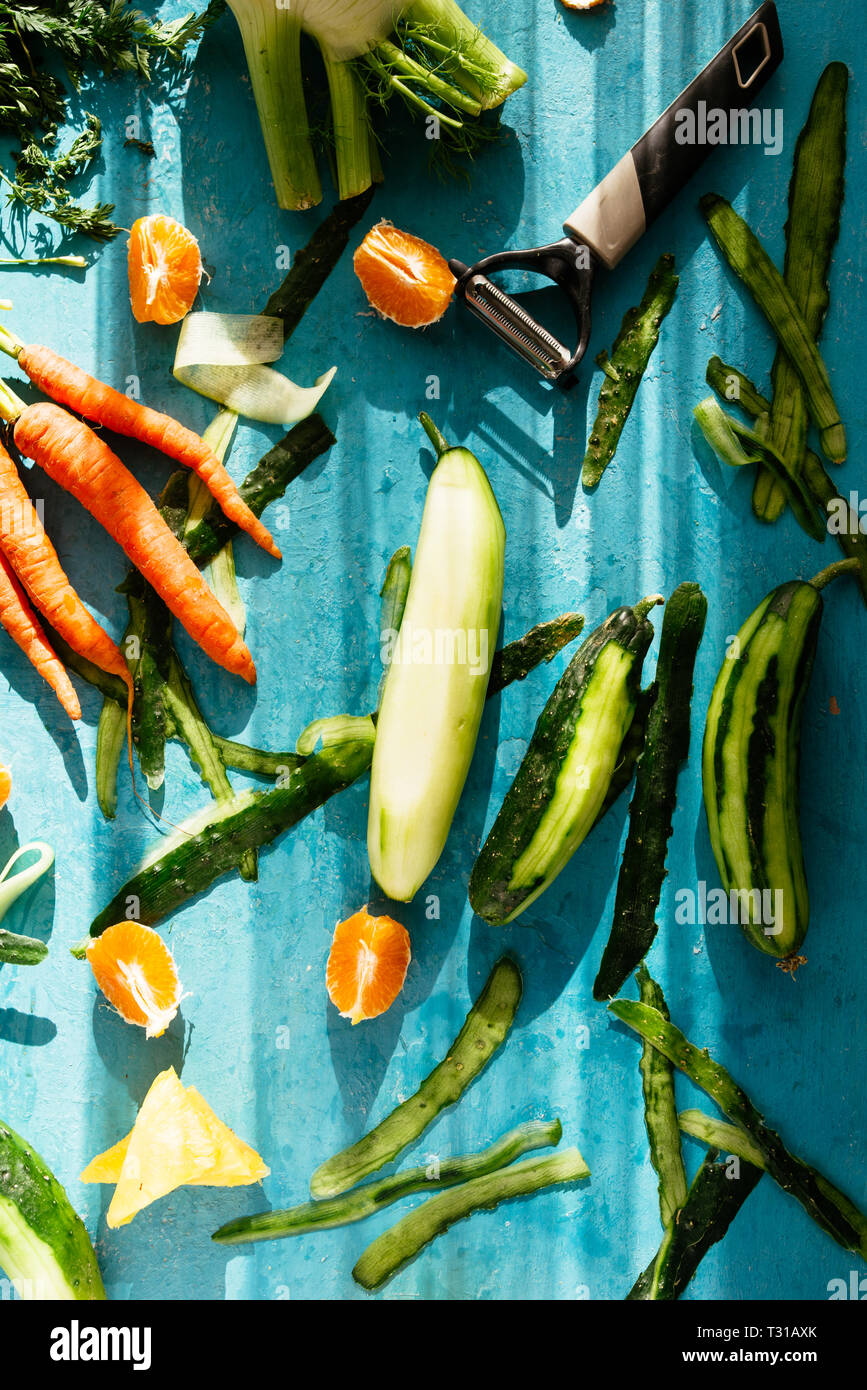 La realizzazione di un fresco succo sano, gli ingredienti vengono preparati e tagliare il cetriolo è pealed con una patata pealer, sopra uno sfondo blu, naturale forte luce Foto Stock