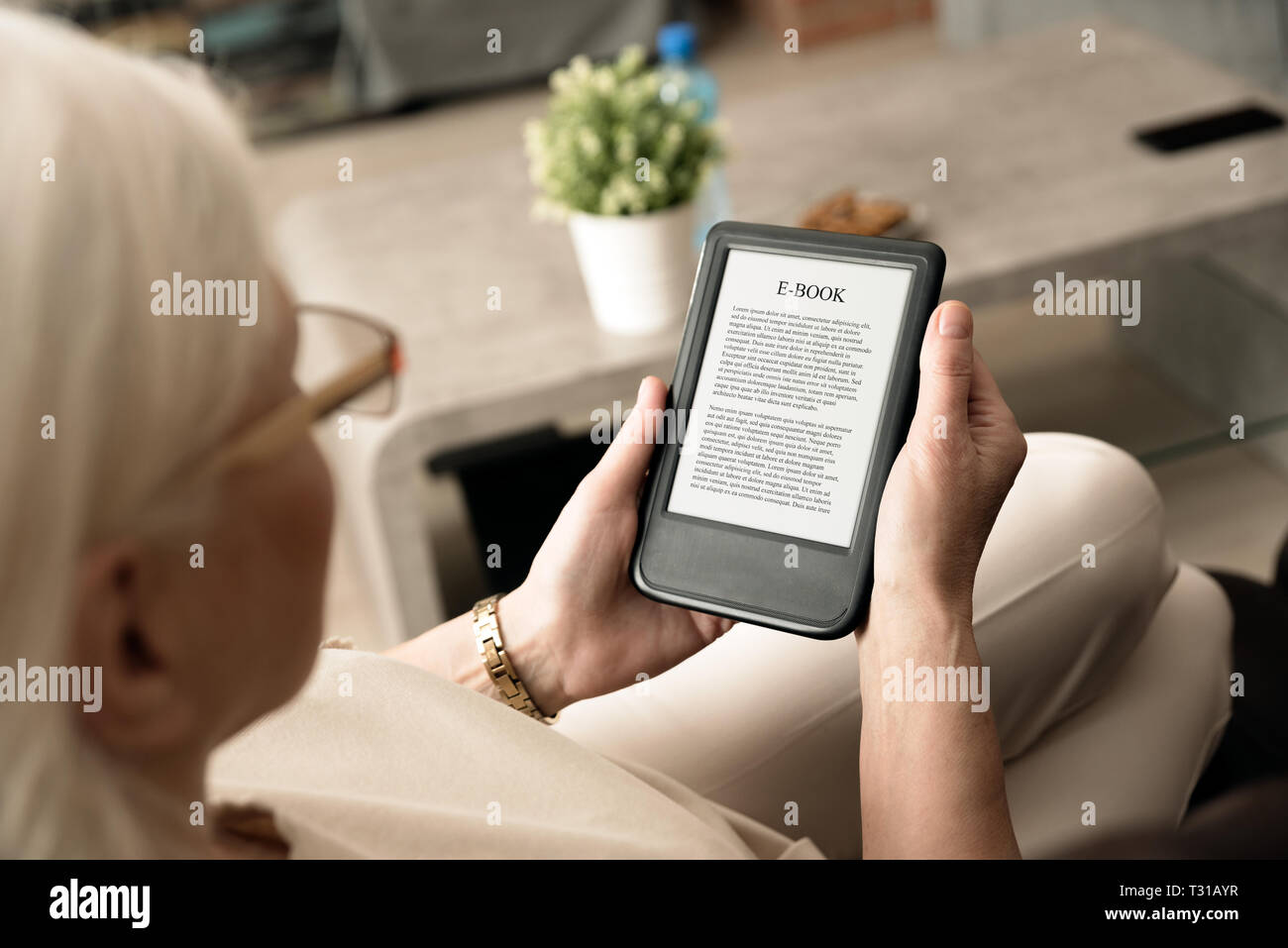 Senior donna seduta dalla finestra, la lettura di un e-book su tavoletta digitale dispositivo Foto Stock
