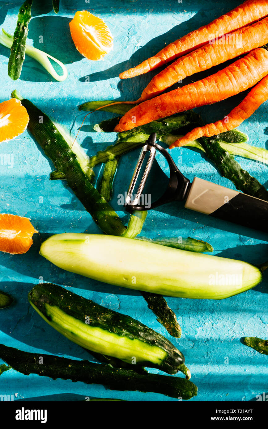 La realizzazione di un fresco succo sano, gli ingredienti vengono preparati e tagliare il cetriolo è pealed con una patata pealer, sopra uno sfondo blu, naturale forte luce Foto Stock