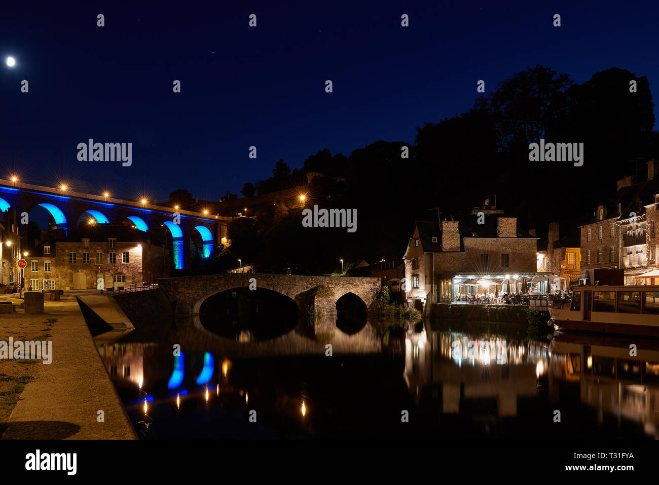 Il pittoresco viadotto, vecchie case di pietra e i ristoranti del porto di Dinan si riflette nell'acqua di notte. Bella illuminazione sotto un cielo stellato. Foto Stock