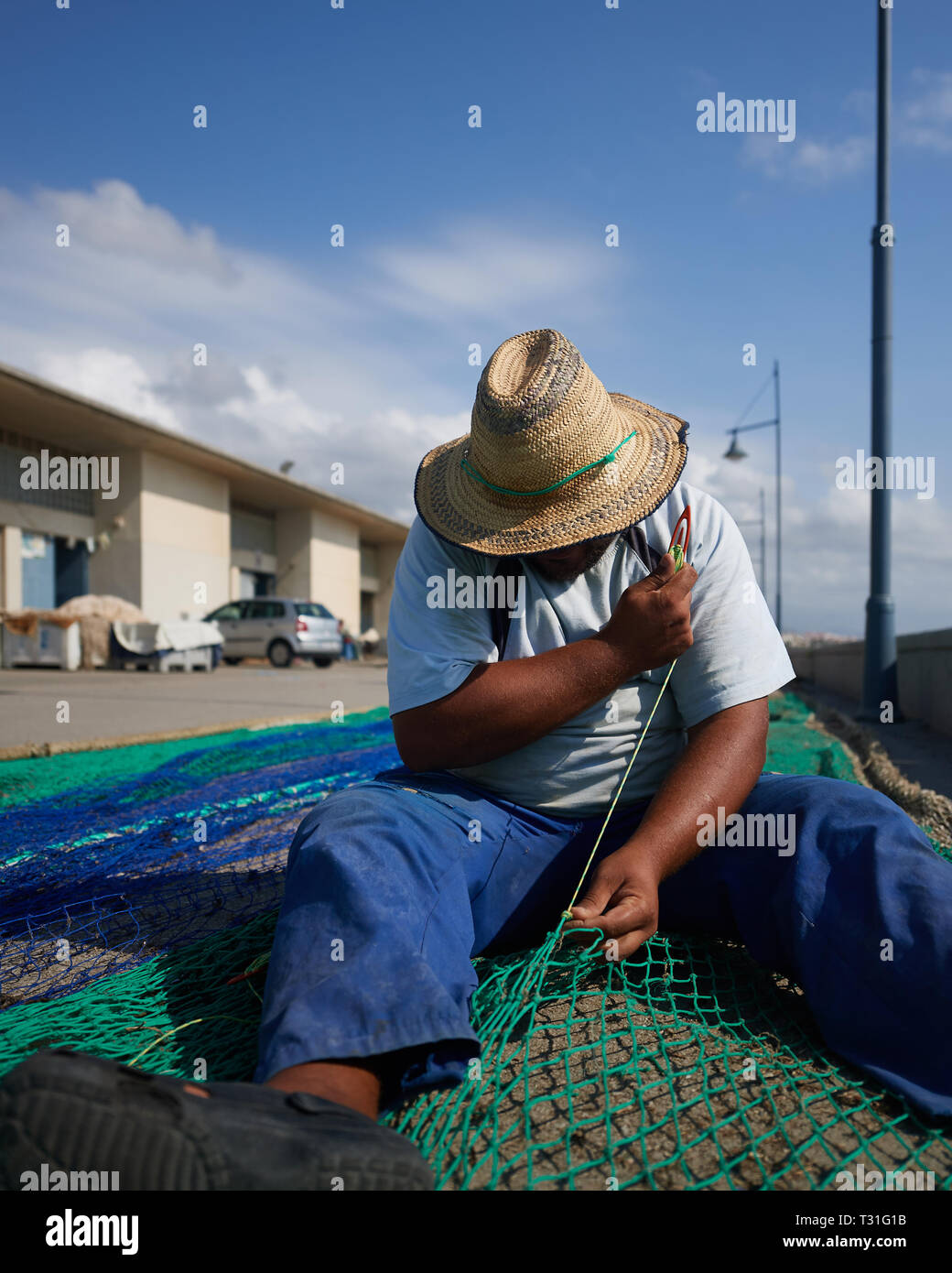 Un pescatore spagnolo in appoggio mentre riassettando le reti a strascico sotto il forte sole di mezzogiorno. Foto Stock