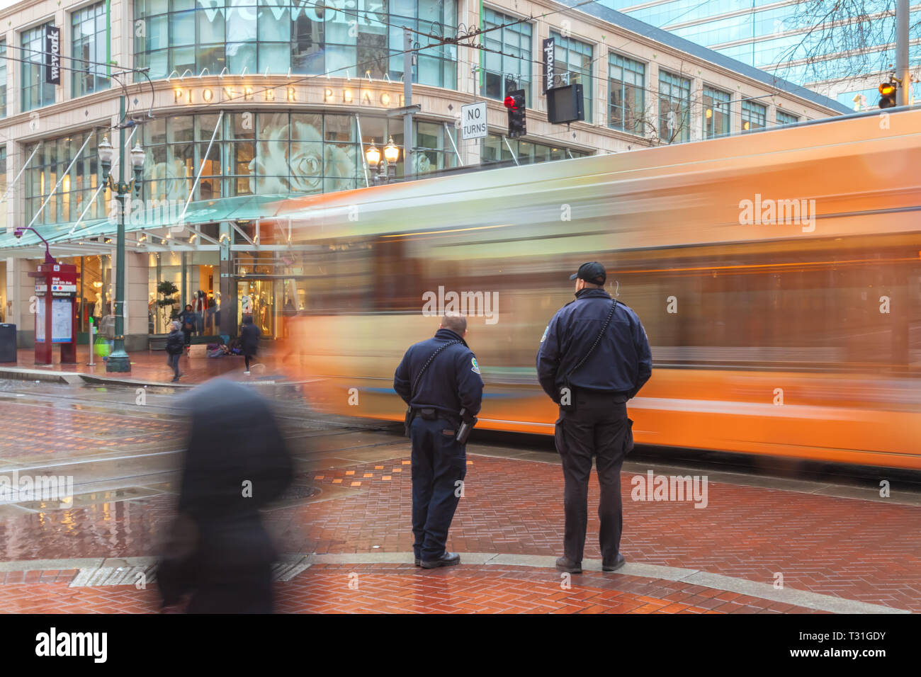 Due ufficiali della polizia stand all'intersezione con un bus in movimento in background, nel centro di Portland, Oregon, Stati Uniti, su una pioggia di mattina. Foto Stock