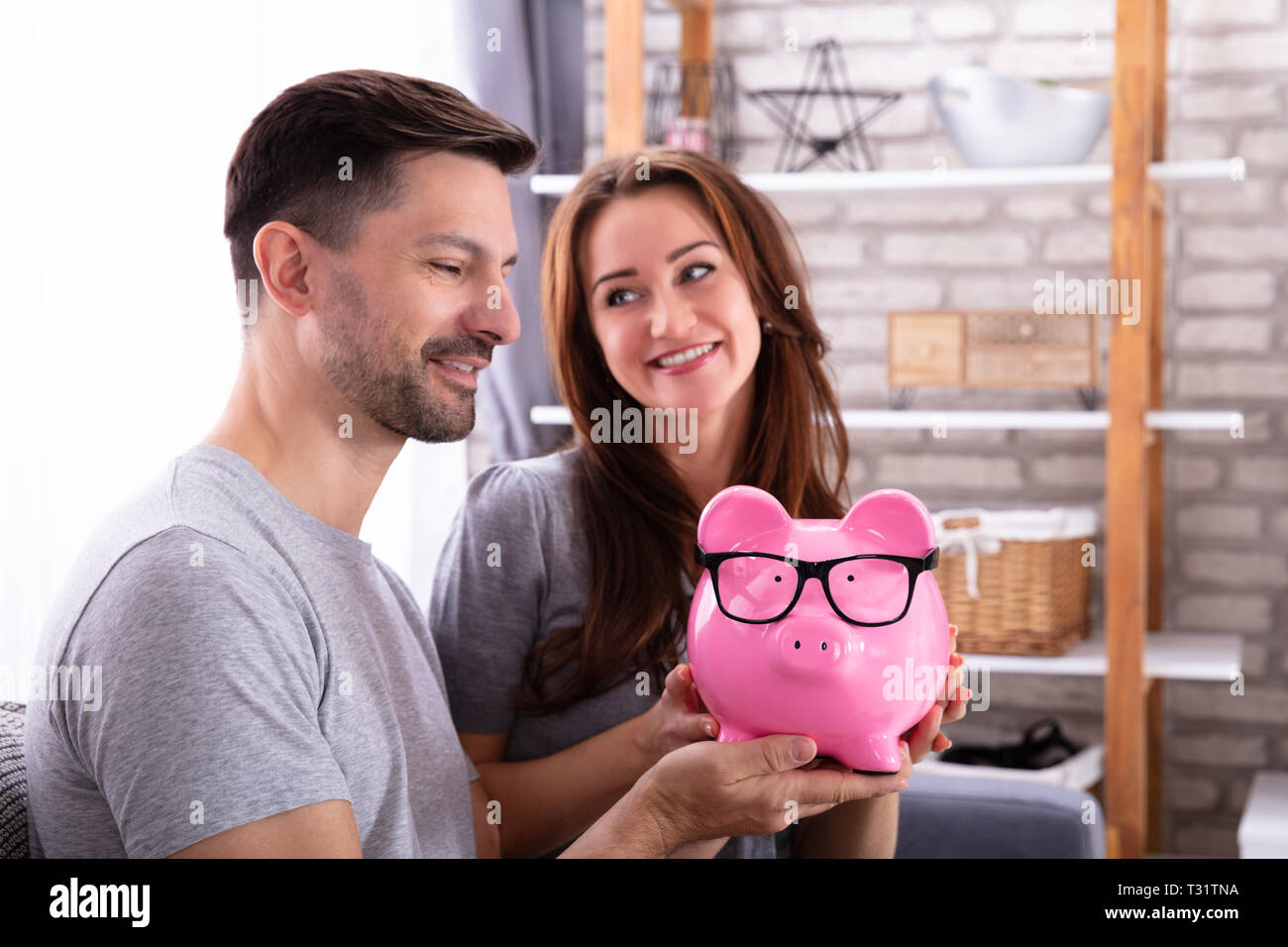 Sorridente Coppia giovane seduto sul divano Azienda Piggybank rosa Foto Stock