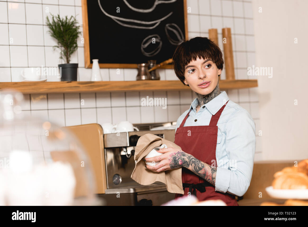 Messa a fuoco selettiva di pretty barista tergi cup mentre sta in piedi vicino alla macchina per espresso Foto Stock