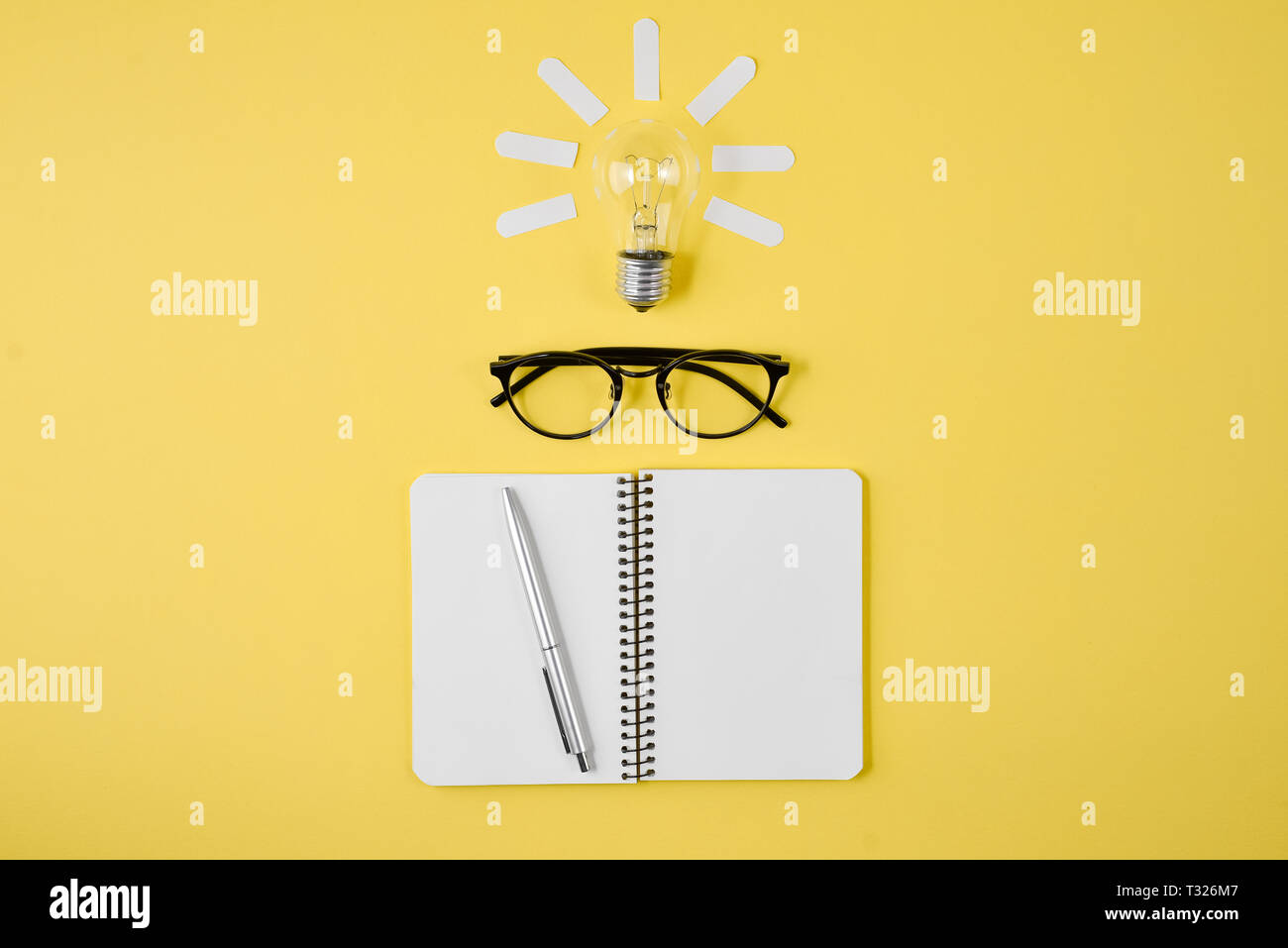 Appartamento laico, vista dall'alto, copia dello spazio. Tabella di pianificazione finanziaria al top con penna, notepad, occhiali e lampadina della luce su sfondo giallo. Concetto il brainstorming Foto Stock