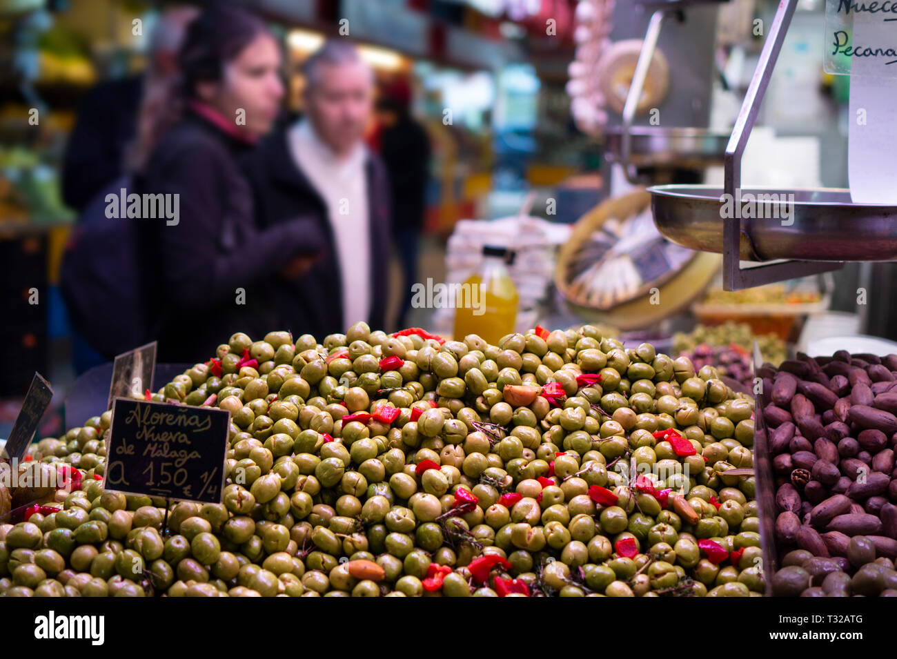 Spanisch geen olive con peperoncino e aglio sott'aceto per la vendita al mercato degli agricoltori in Spagna Malaga con i clienti sfocata Foto Stock
