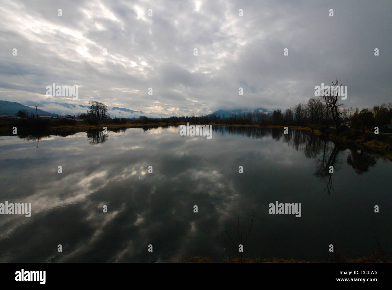 Una placida backwater del fiume di Vedder riflette un cielo grigio turbolento coperto in Chilliwack, Columbia Britannica, Canada Foto Stock